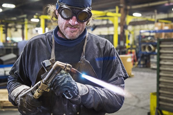 Caucasian welder adjusting blowtorch in factory