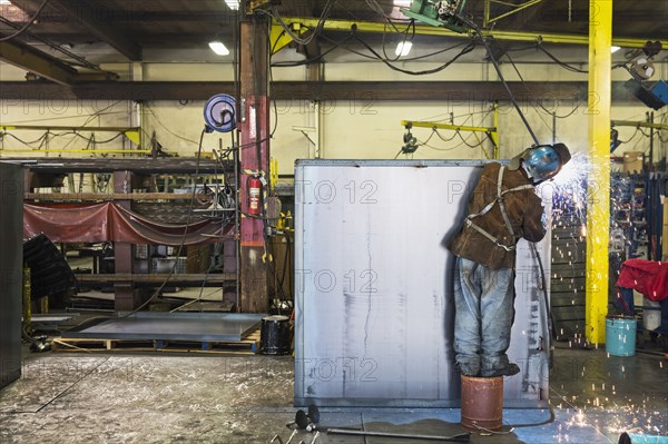 Asian worker grinding metal container in factory