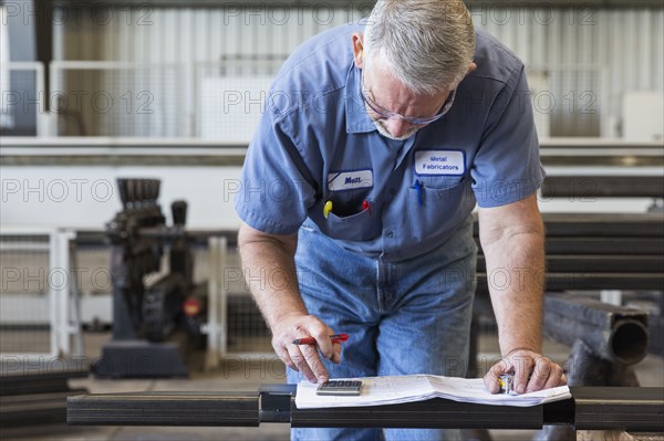 Caucasian worker using calculator in factory