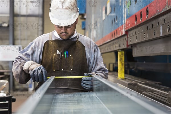 Pacific Islander worker measuring metal in factory