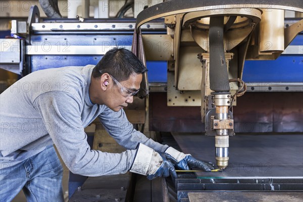 Asian worker fabricating metal in factory