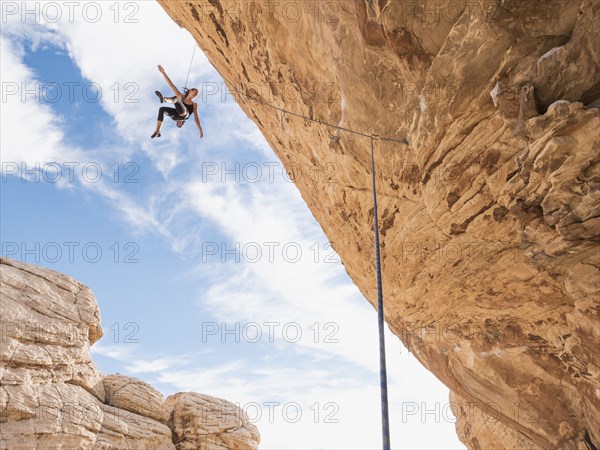Mixed Race girl hanging from rope while rock climbing