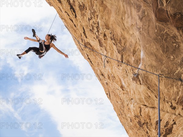 Mixed Race girl hanging from rope while rock climbing