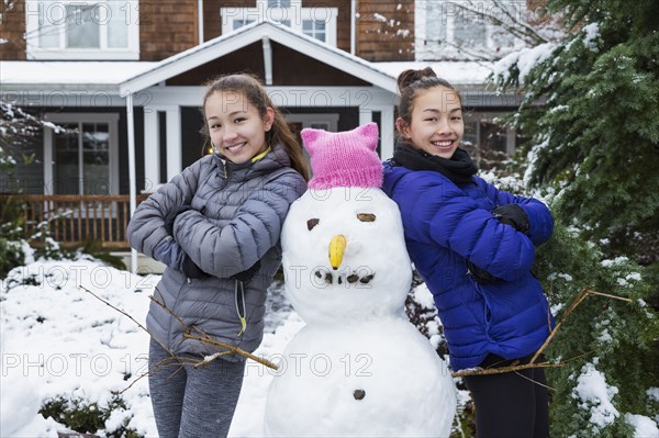 Mixed Race girls posing with snowman wearing pink hat with ears