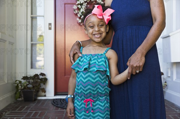 Smiling mixed race mother and daughter standing on front stoop