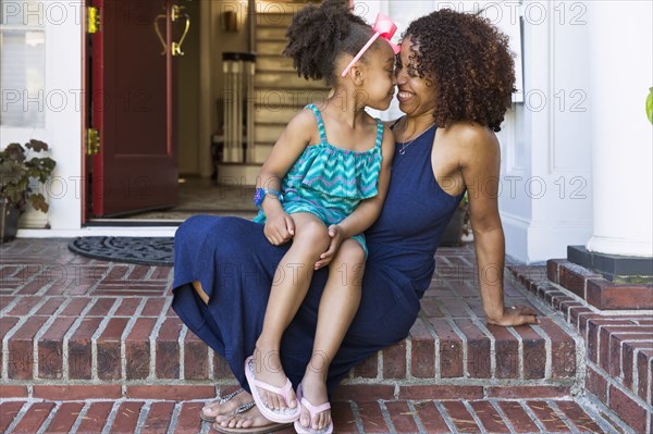 Smiling mixed race mother and daughter rubbing noses on front stoop