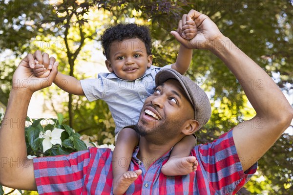 Smiling mixed race father carrying baby son on shoulders