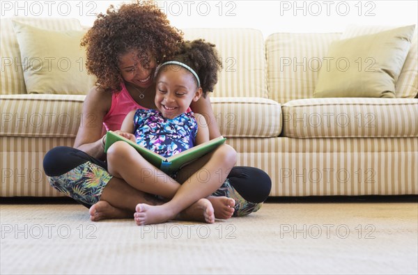 Mixed race mother and daughter reading book on floor near sofa