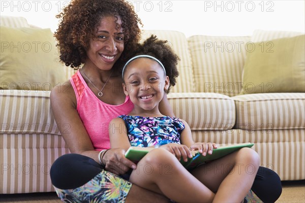 Mixed race mother and daughter reading book on floor near sofa