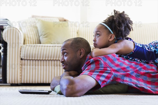 Mixed race father and daughter laying on floor watching television