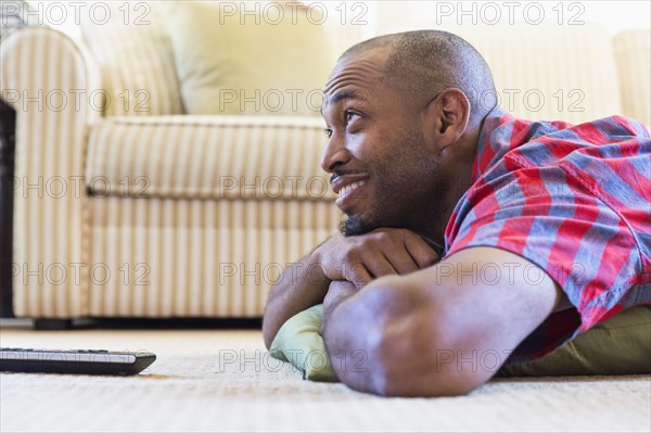 Mixed race man laying on floor watching television