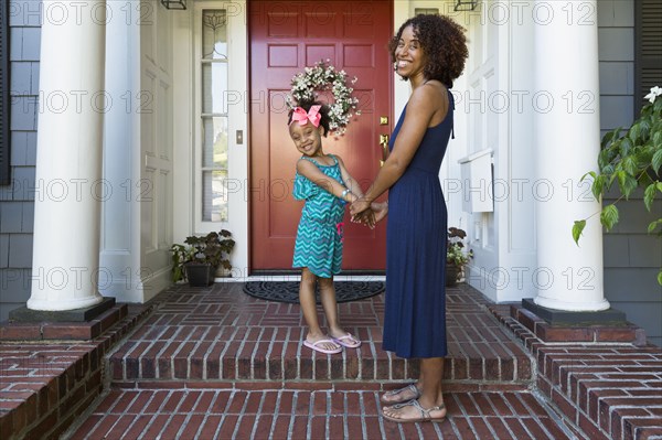 Portrait of smiling mixed race mother and daughter on front stoop