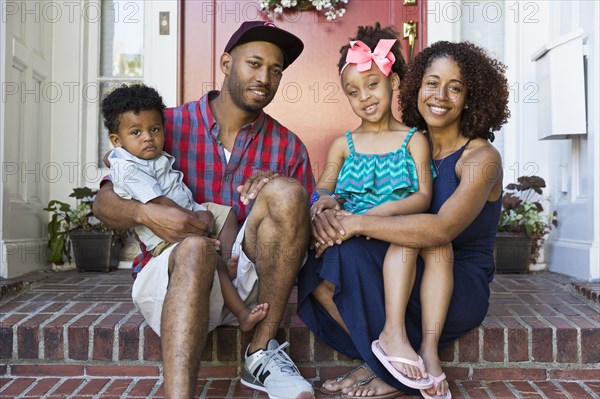 Portrait of smiling mixed race family sitting on front stoop