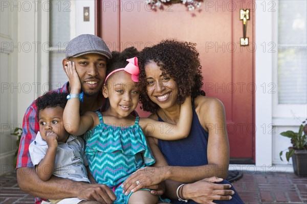 Portrait of smiling mixed race family sitting on front stoop