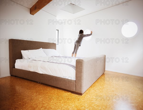 Mixed race girl looking out window in modern bedroom