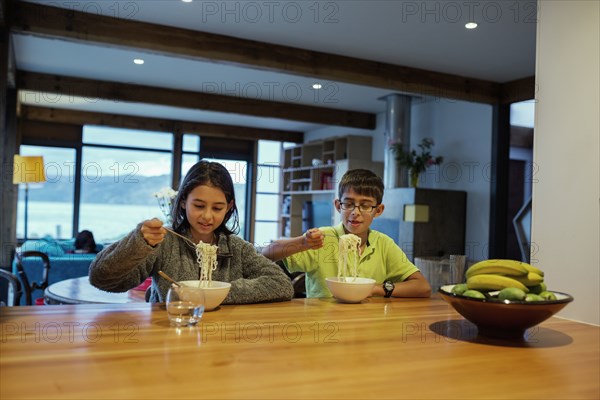 Mixed race children eating noodles at table