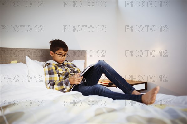 Mixed race boy reading magazine in bedroom