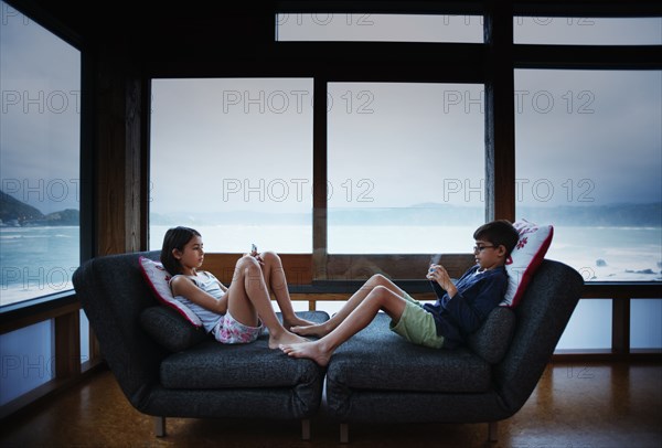 Mixed race children using cell phones in living room