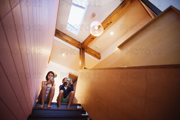 Mixed race children using cell phones on staircase