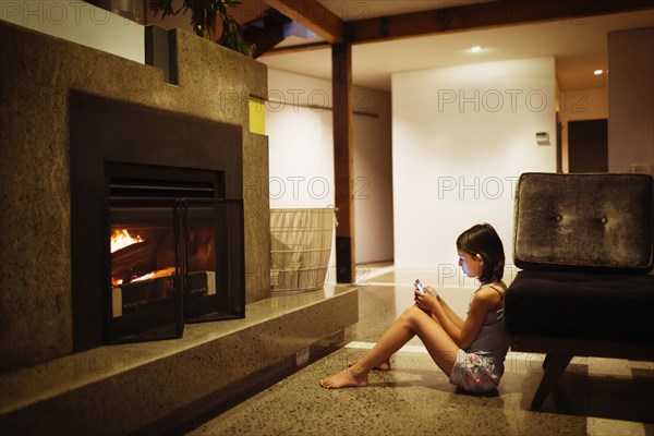 Mixed race girl using cell phone near fireplace in living room