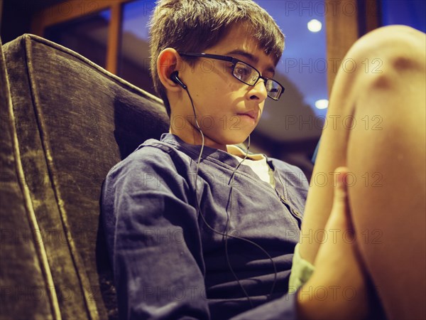 Mixed race boy listening to earbuds on sofa