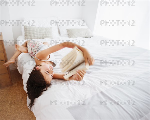 Mixed race girl reading book on bed