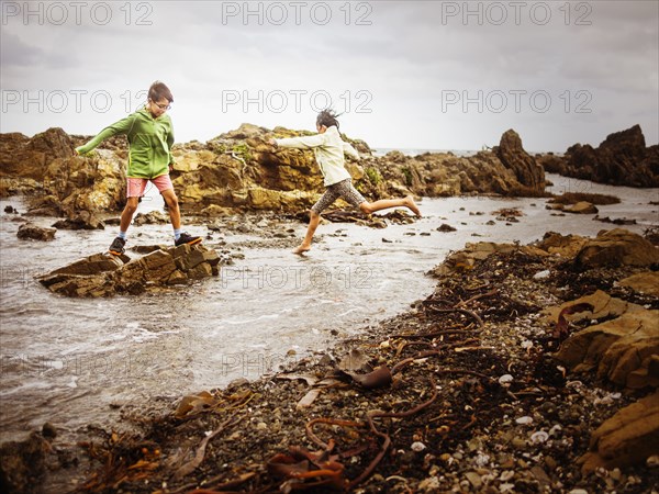 Mixed race brother and sister playing on rocky beach