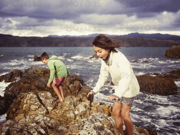 Mixed race brother and sister playing on rocky beach