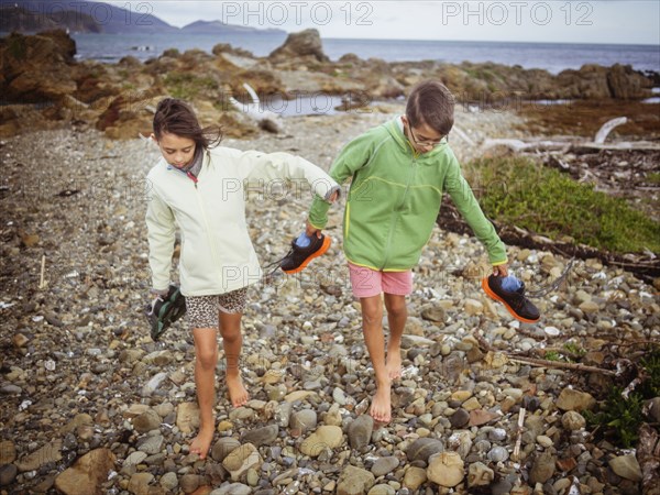 Mixed race brother and sister carrying their shoes on rocky beach