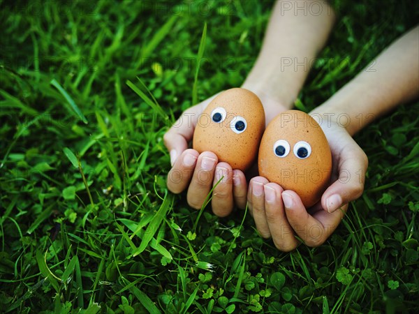 Close up of mixed race girl holding eggs with googly eyes