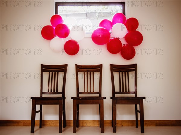 Bunches of colorful balloons over chairs near wall