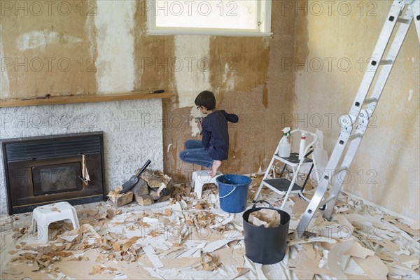 Mixed race boy stripping wallpaper in living room
