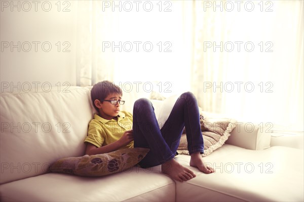 Mixed race boy reading book on living room sofa