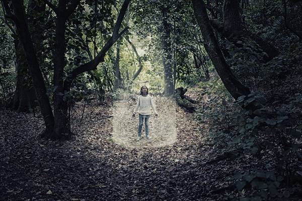 Mixed race girl standing in beam of light in forest