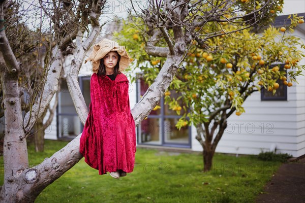 Mixed race girl in witch costume sitting in tree