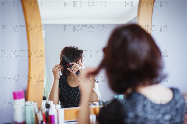 Mixed race woman straightening hair in mirror