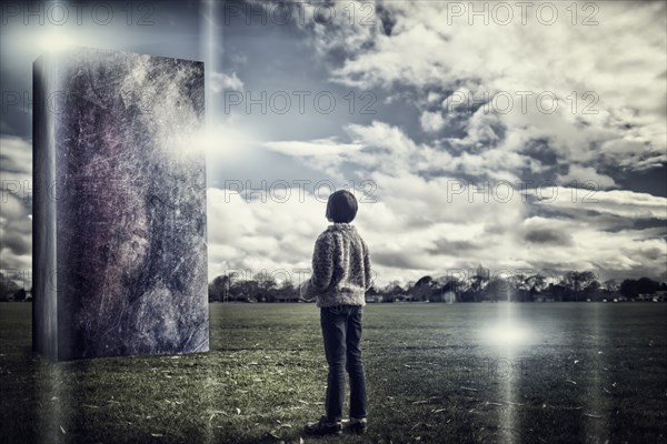 Mixed race girl admiring stone sculpture in field