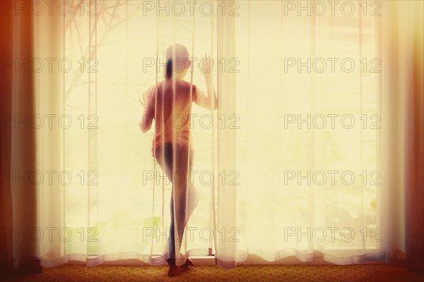 Mixed race girl behind curtain looking out window