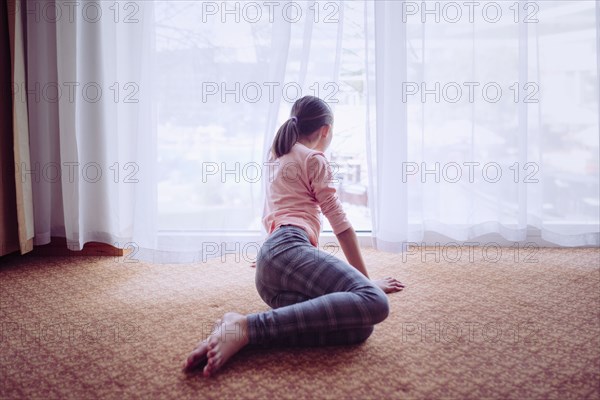 Mixed race girl sitting on floor looking out window