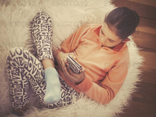 Mixed race girl using cell phone on in furry chair