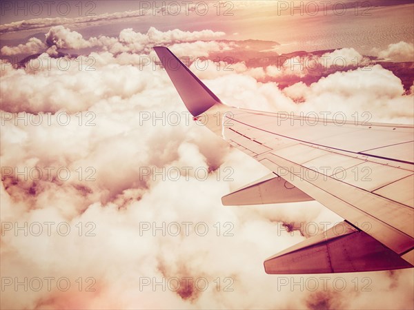 Aerial view of airplane wing flying over clouds in sky