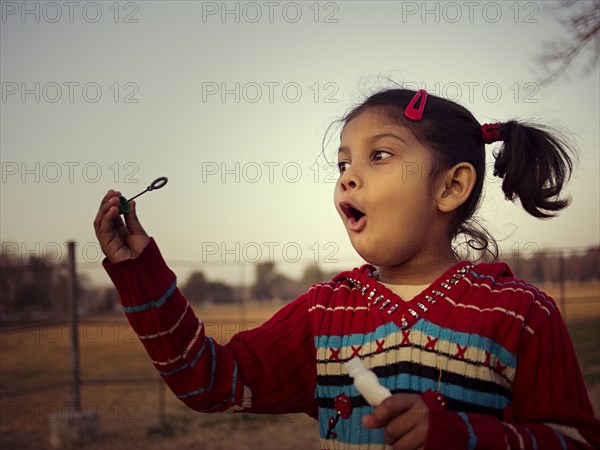 Mixed race girl blowing bubbles in field