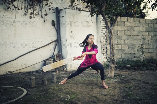 Mixed race girl playing cricket near wall