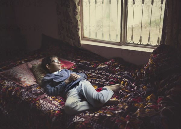 Mixed race boy looking out bedroom window