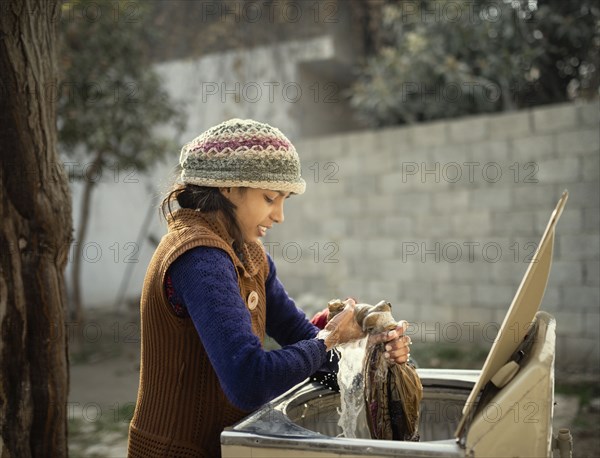 Woman in knit hat hand-washing clothing outdoors