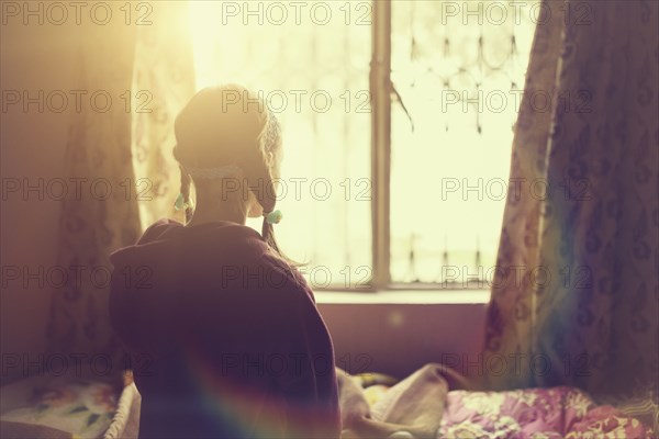 Mixed race girl looking out bedroom window