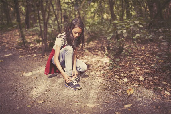 Mixed race girl tying shoelaces on dirt path