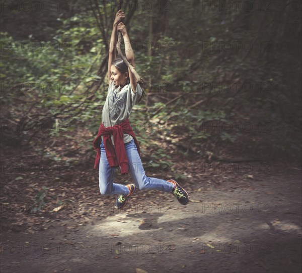 Mixed race girl swinging from tree branch on dirt path