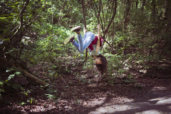 Mixed race girl swinging from tree branch on dirt path