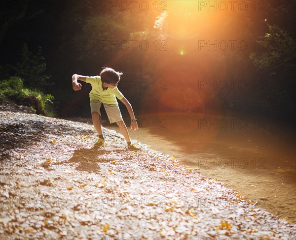 Mixed race boy skipping stones in stream